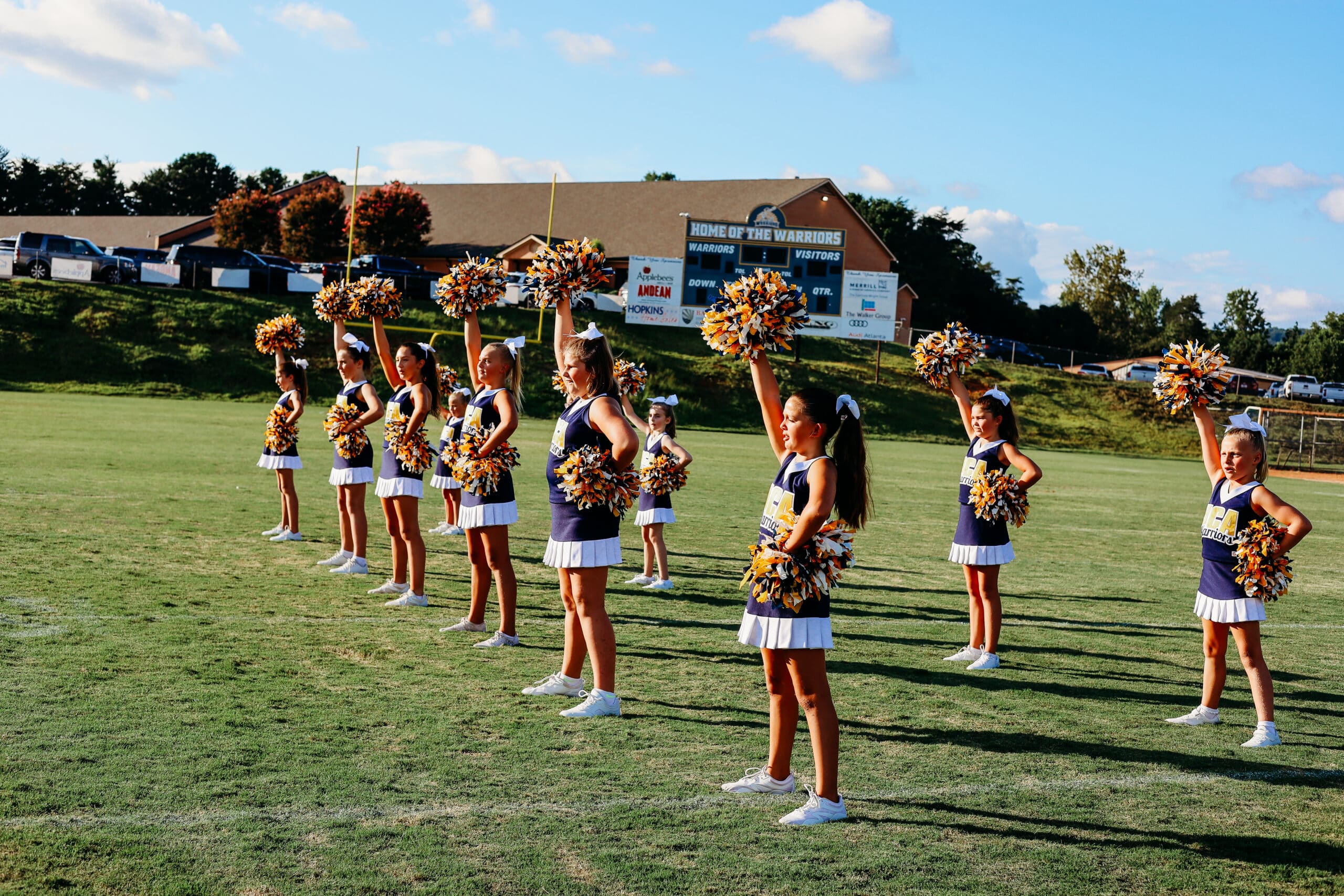 HCA middle school cheerleaders on field in uniforms with pom poms