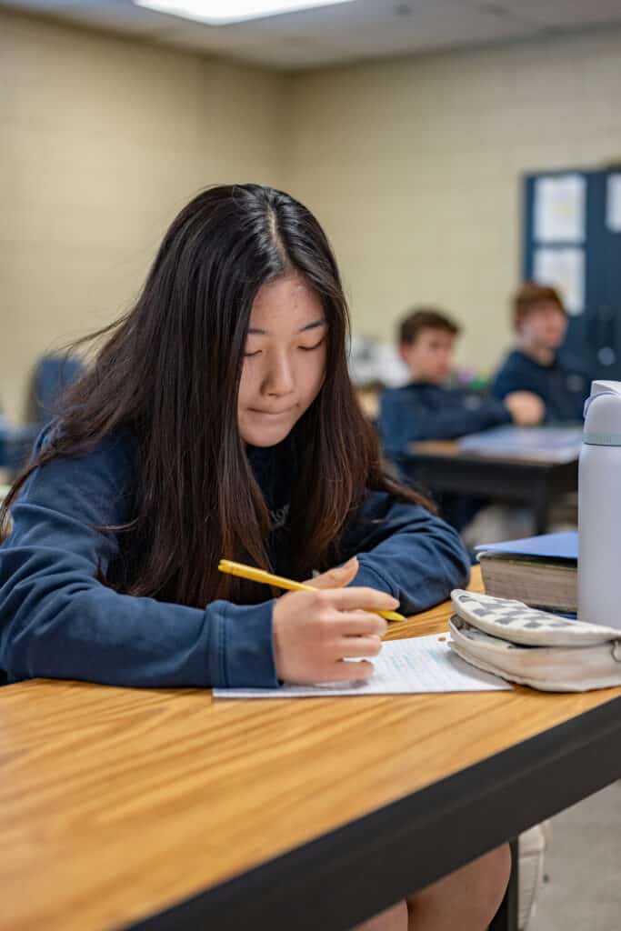 HCA High School student holding pencil and looking at paper on desk