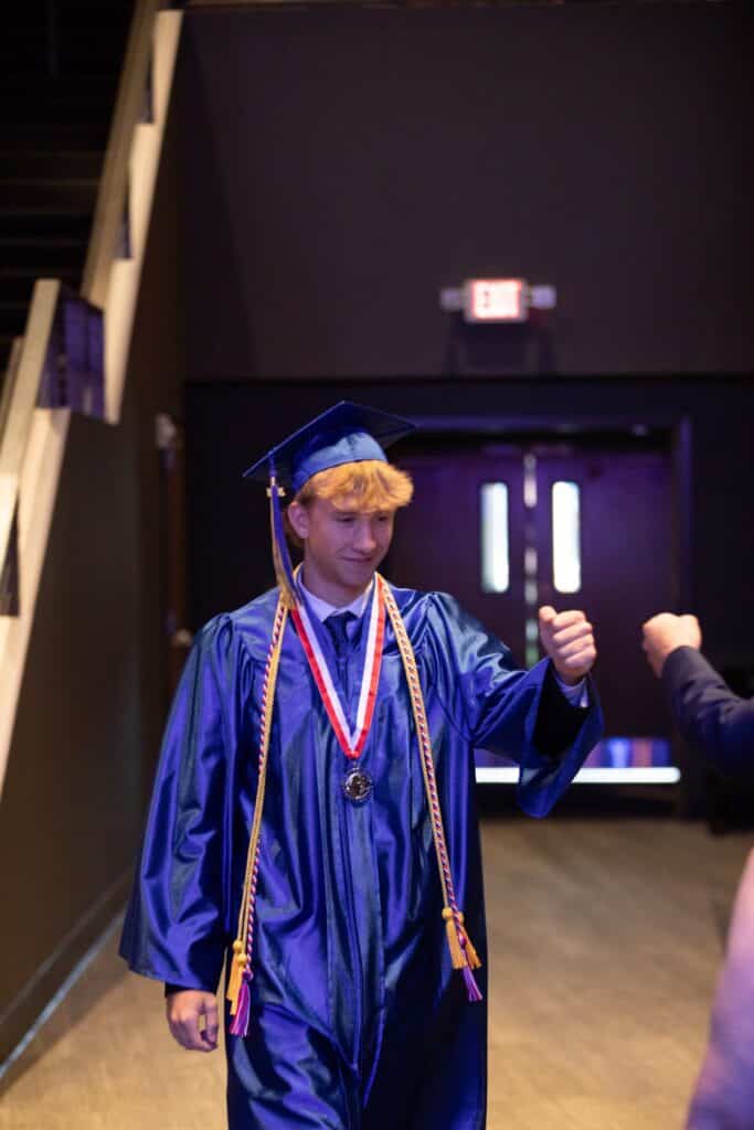 HCA graduate in cap and gown giving fist bump
