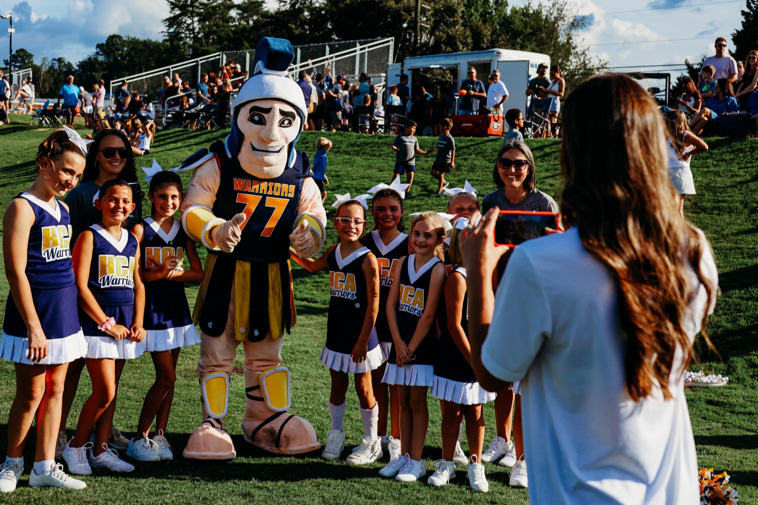 HCA mascot and cheerleaders smiling and posing for photo on field